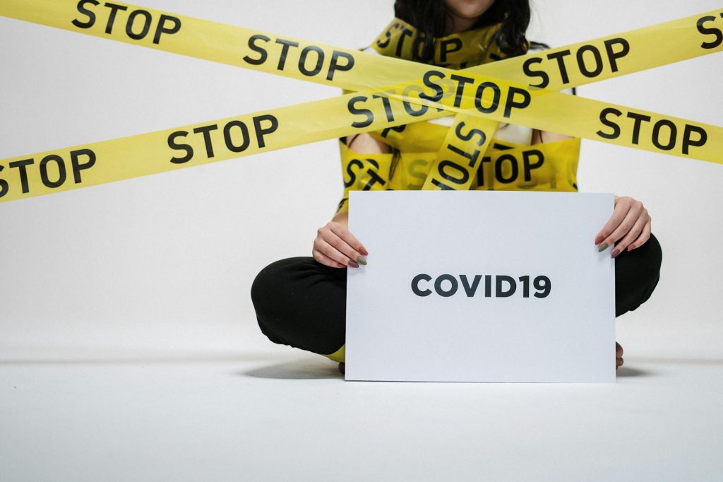 A woman holding a sign saying Covid-19 with lots of "Stop" tape over her